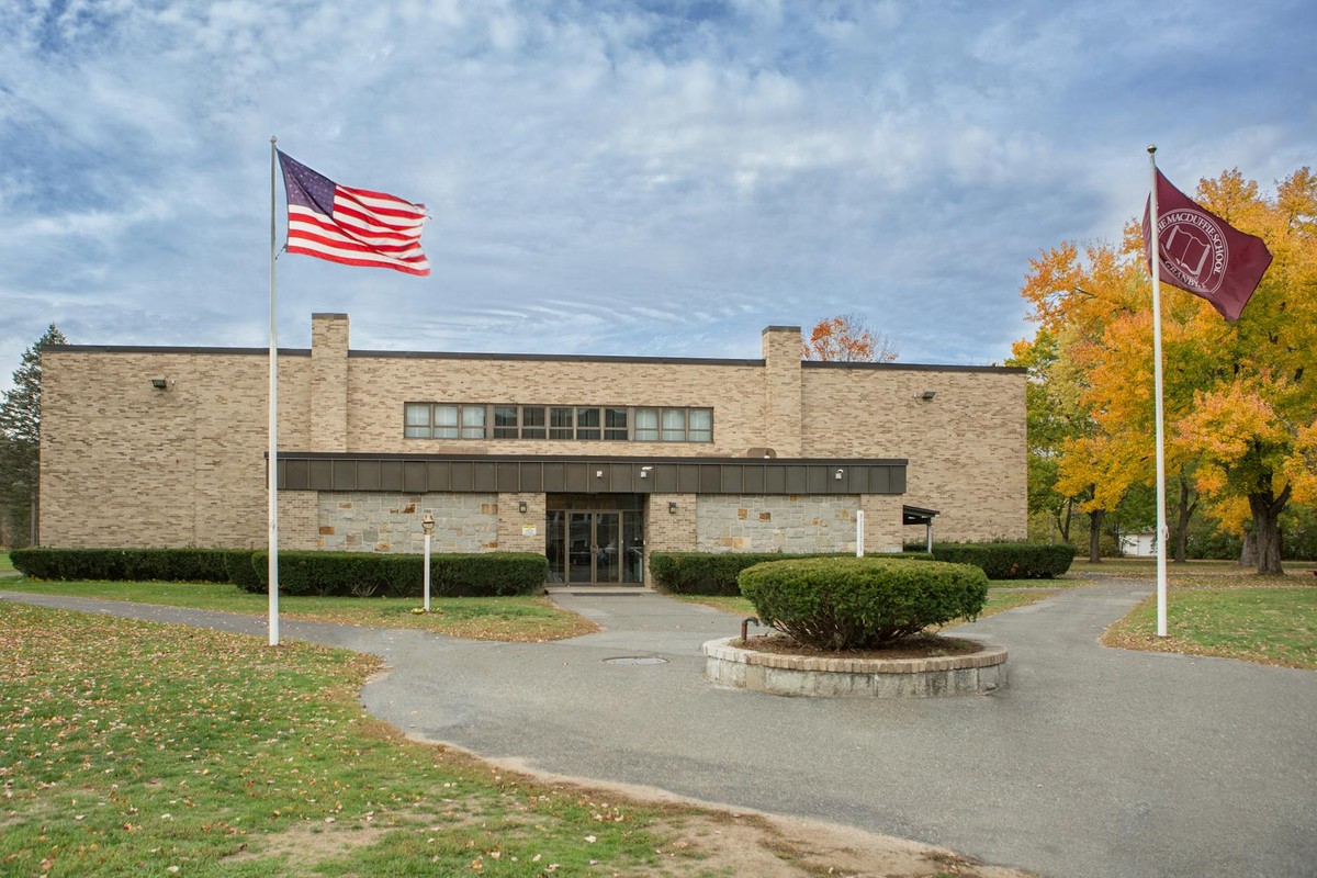 A university campus building with American and school flags set amidst colorful autumn trees.
