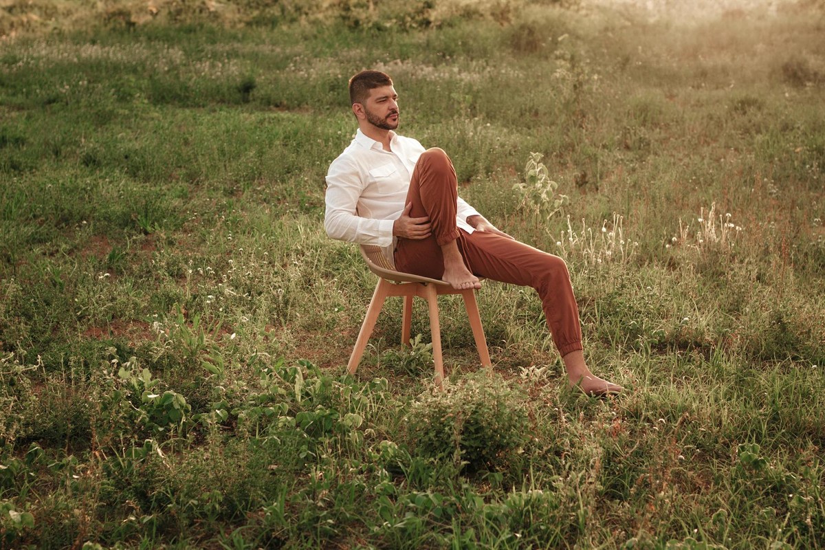 A man sits barefoot on a chair in a sunlit meadow, Barreiras, Brazil.