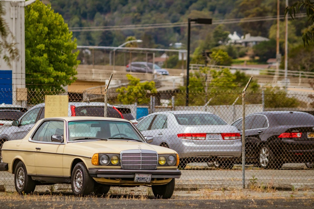 Classic Mercedes Benz parked in a fenced urban parking area with various cars in background.