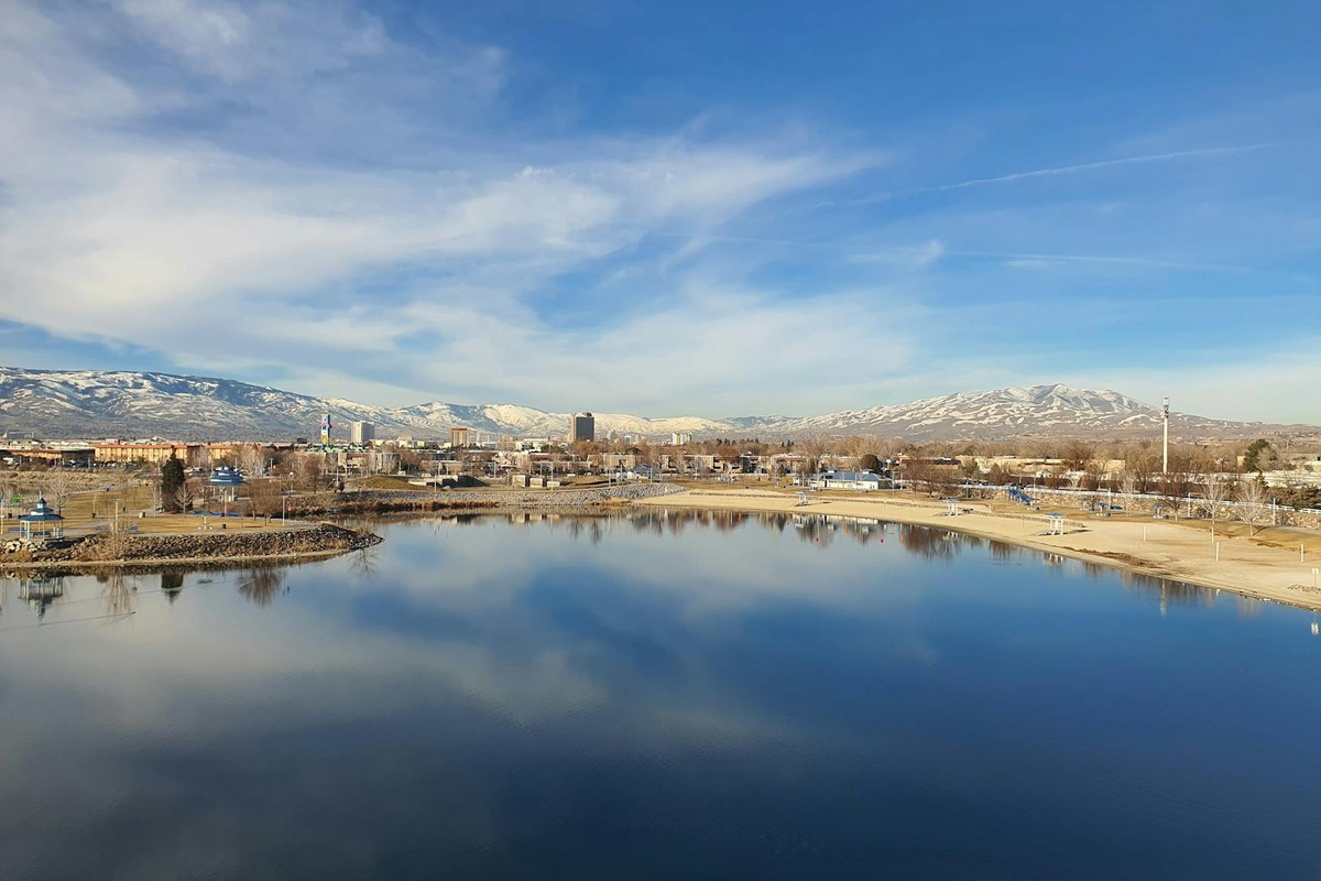 Discover Reno's skyline reflecting on a tranquil lake with snow-capped Sierra Nevada mountains in the background.
