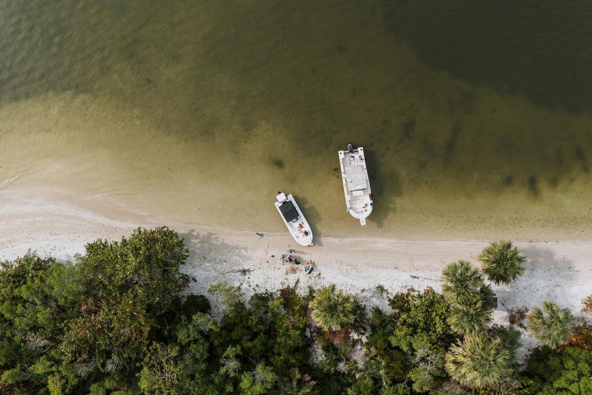 Drone shot of boats moored on the sandy shore of Lakewood Park, FL, with lush trees and clear waters.