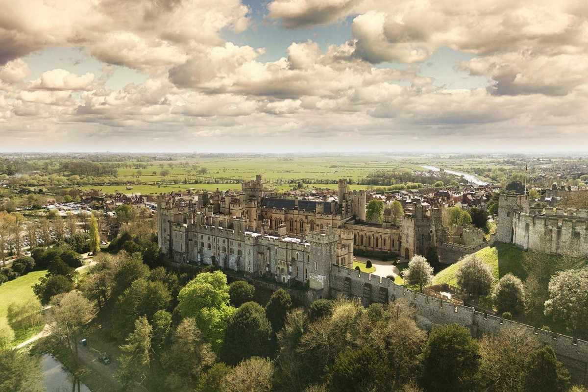 A breathtaking aerial shot of Arundel Castle surrounded by lush greenery and under a dramatic sky.
