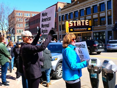 People protesting outside a small town theater with signs about social issues.