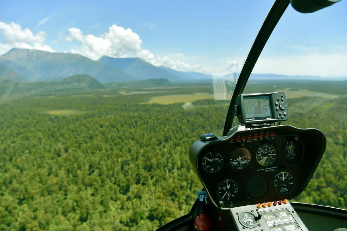 Scenic aerial view from a helicopter cockpit over lush forests in Haast, New Zealand.
