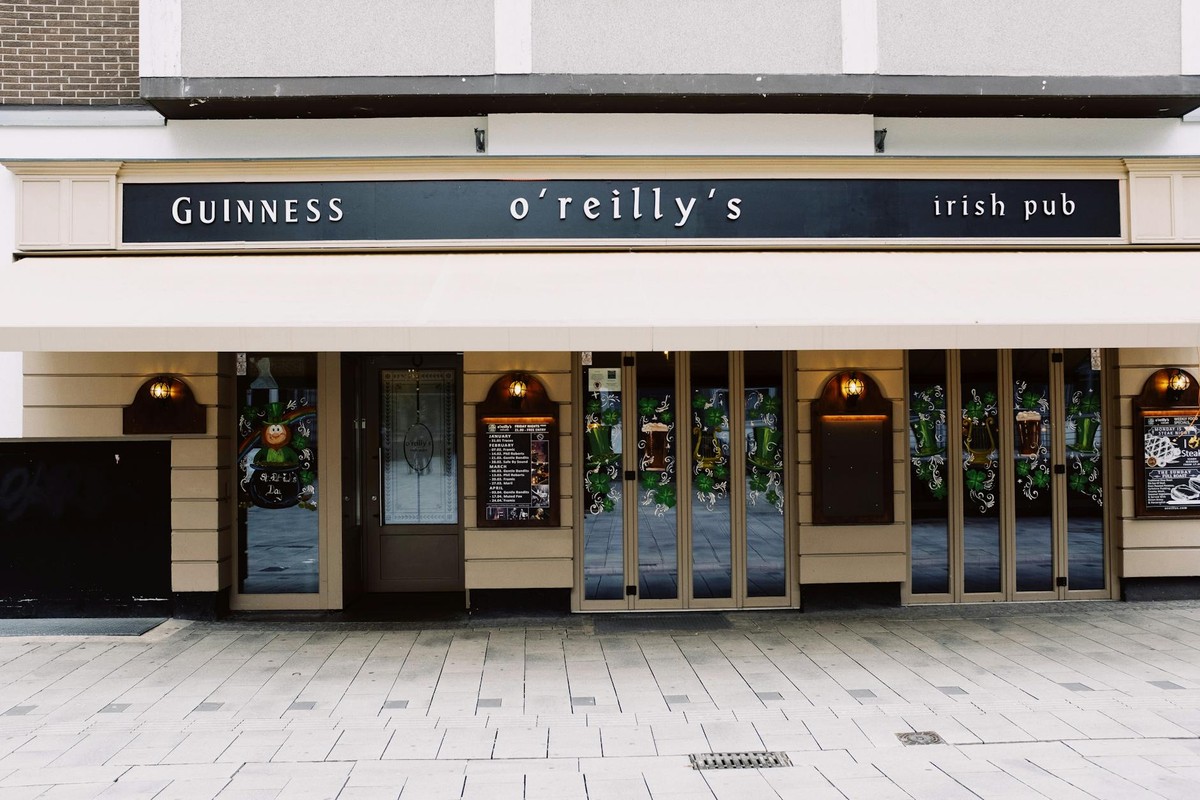 Exterior of modern bar building with mirrored windows decorated with wide signboard and menu on chalkboards below lanterns in street