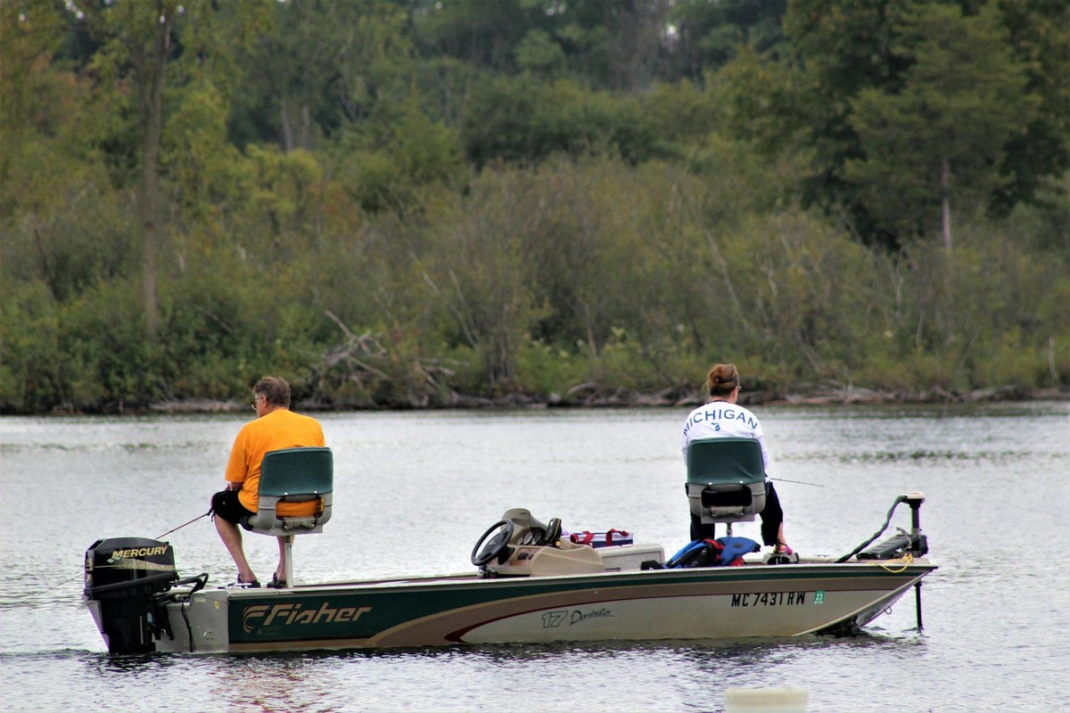 A couple leisurely fishing on a Michigan lake from a motorboat, surrounded by nature.