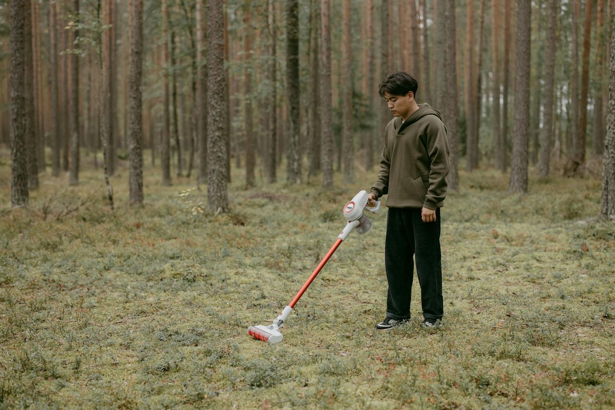 An adult man with a vacuum cleaner in a forest setting, capturing modern living concepts.