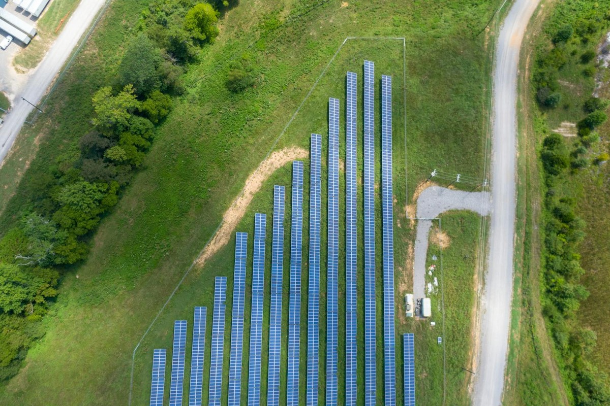 Aerial view showing a solar panel array in a lush rural landscape with a road.