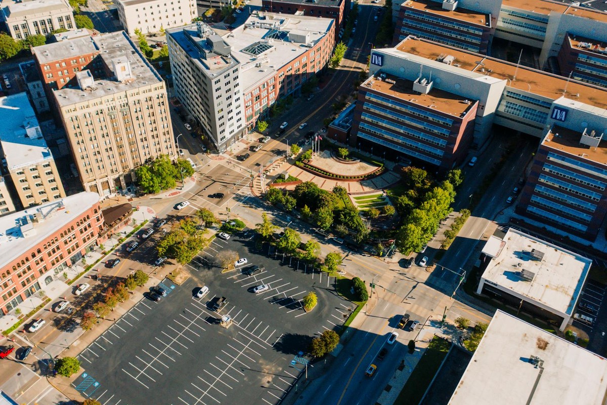 Drone view of cityscape with asphalt roads running between modern multistory buildings and parking area on sunny day