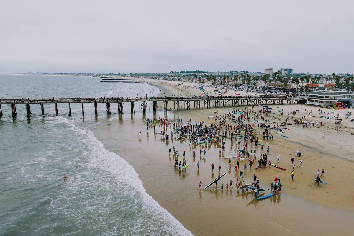 Aerial shot of a bustling beach day at Newport Beach Pier, capturing the lively summer scene.