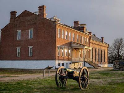 A historical cannon in front of a brick building at Fort Smith, Arkansas, during sunset.