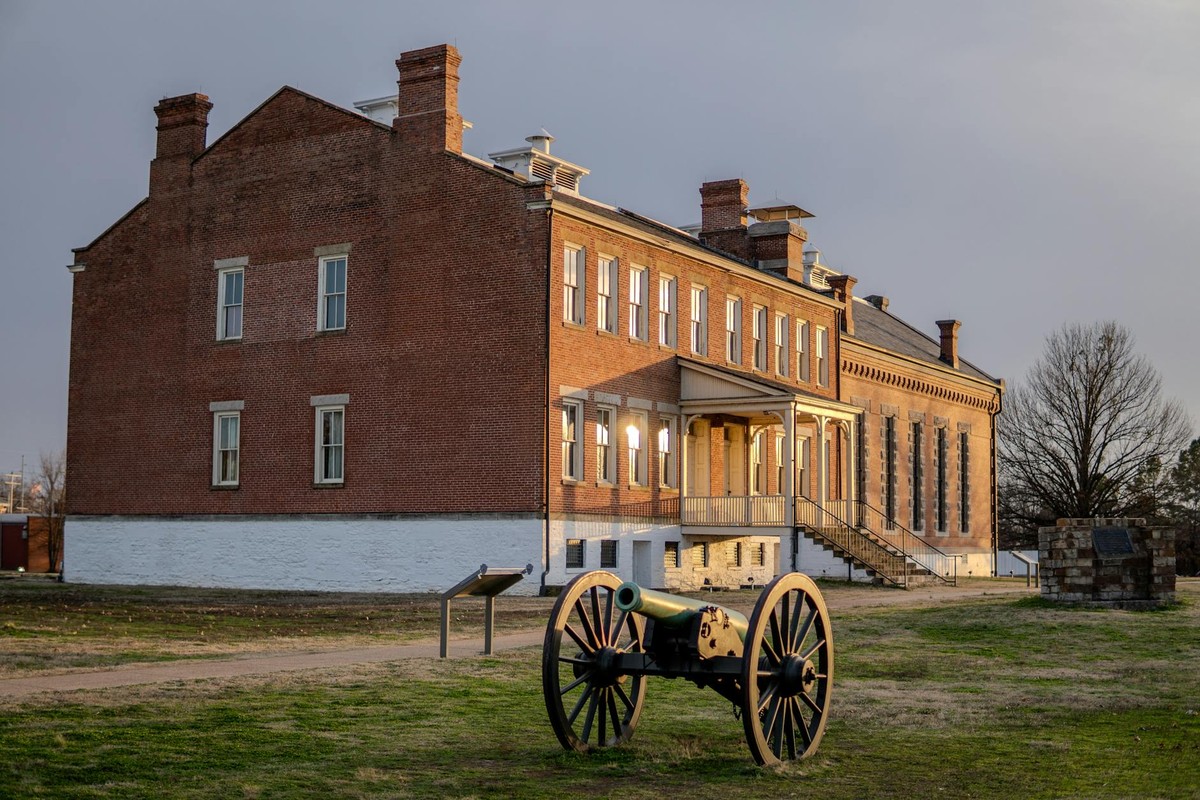 A historical cannon in front of a brick building at Fort Smith, Arkansas, during sunset.