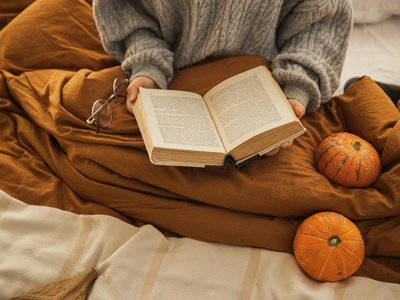 A person reading a book in a cozy setting with pumpkins, embodying autumn relaxation.