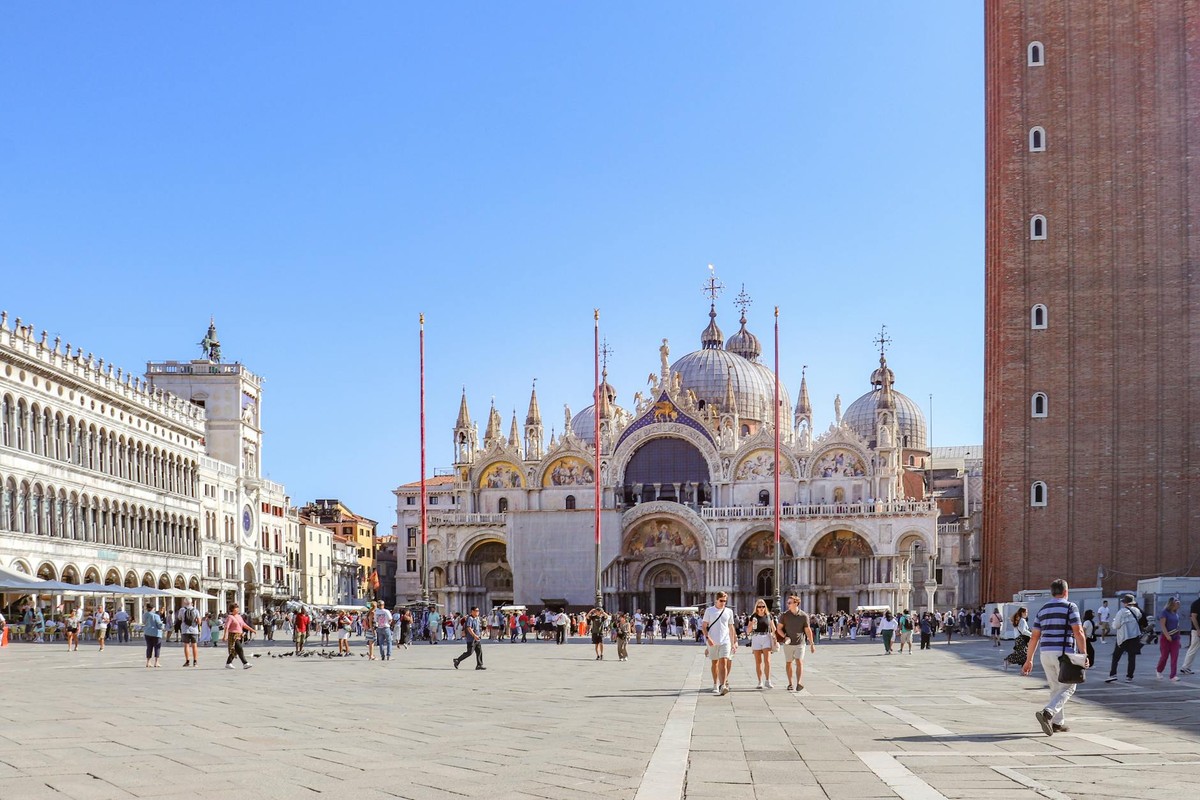 Tourists explore St. Mark's Square near the iconic St. Mark's Basilica on a sunny day in Venice, Italy.