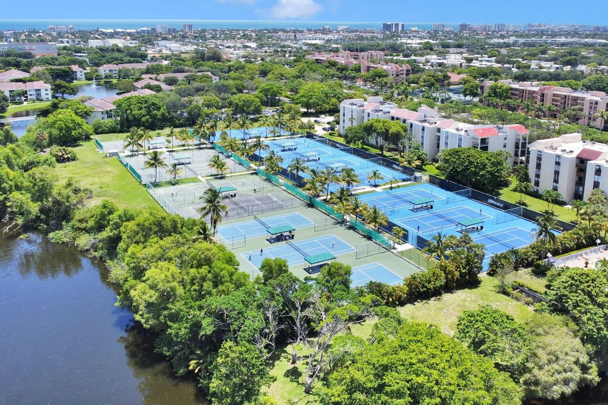 Aerial shot of tennis courts surrounded by lush greenery, apartments, and a river.