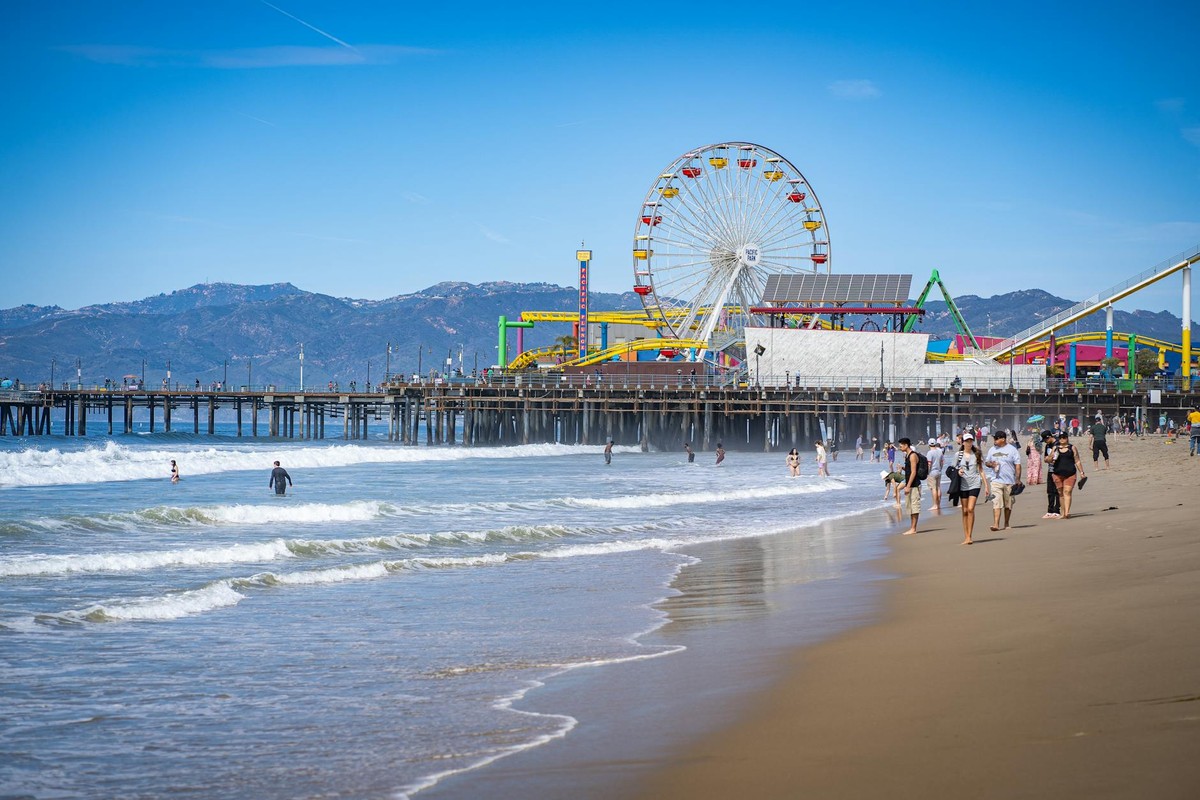 Scenic view of Santa Monica Pier with Ferris wheel, beach, and people enjoying a sunny day.