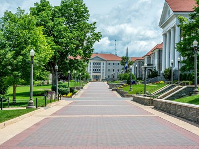 Scenic view of a beautifully landscaped college campus with historic buildings and a tree-lined pathway.