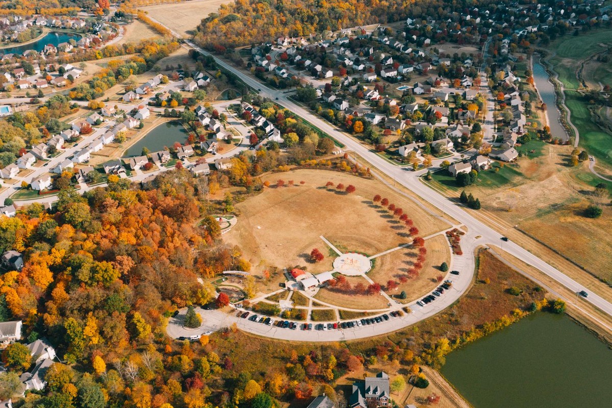 Drone view of bright lawn with colorful trees near residential building roofs and water channel with road in fall