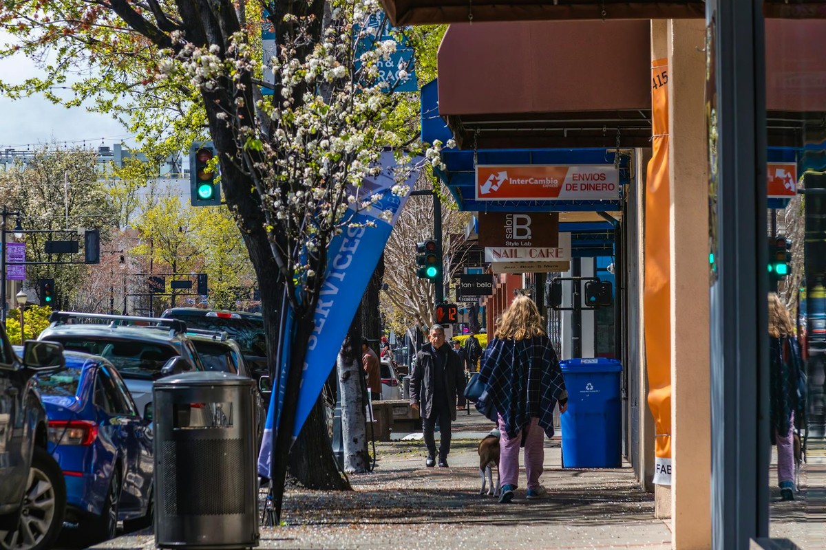 Vibrant urban scene showing people walking on a busy street lined with cars and storefronts.
