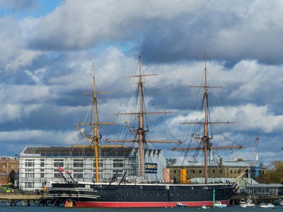 A majestic historic ship anchored at Portsmouth Harbor with a cloudy sky backdrop.