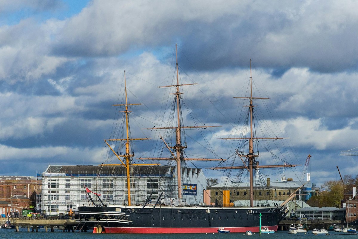 A majestic historic ship anchored at Portsmouth Harbor with a cloudy sky backdrop.