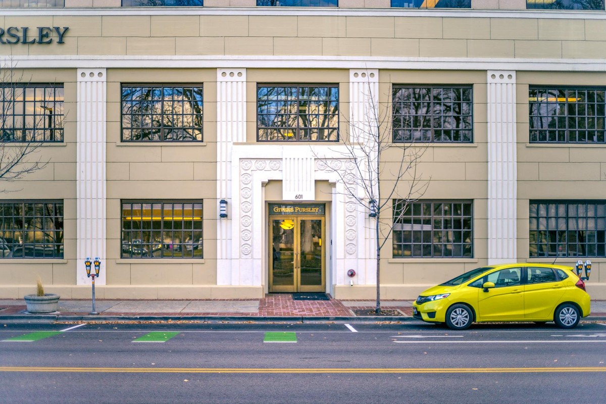 Yellow hatchback car parked on asphalt road near modern building with symmetric windows in city