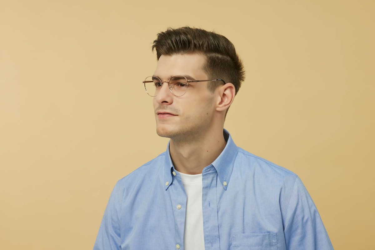 Portrait of a young man wearing eyeglasses and a blue shirt, looking serious against a neutral background.