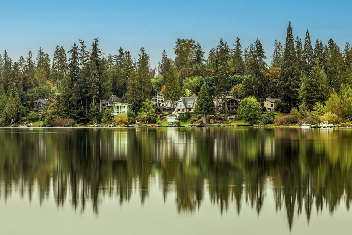 Scenic view of lakefront homes and evergreen trees reflecting in calm waters of Renton, WA.