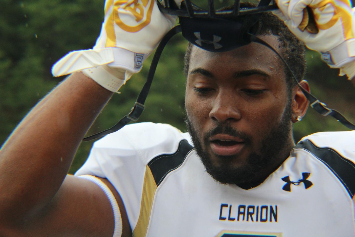 Close-up of a football player adjusting his helmet mid-game, showcasing focus and athleticism.