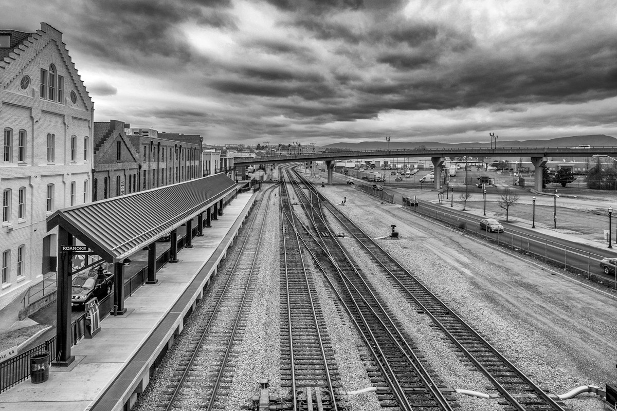 Grayscale view of railroad tracks at Roanoke railway station under dramatic cloudy skies.