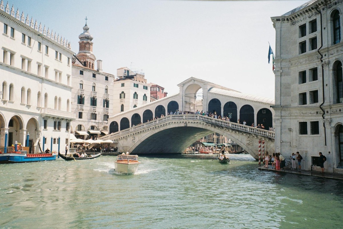 Rialto Bridge over the Grand Canal in Venice, bustling with tourists under a sunny sky.