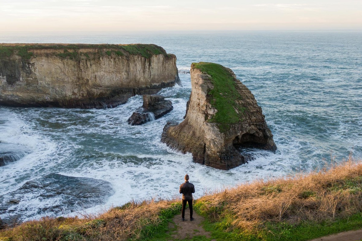 A lone man gazes at the waves crashing against Shark Fin Cove in Davenport, CA, USA.
