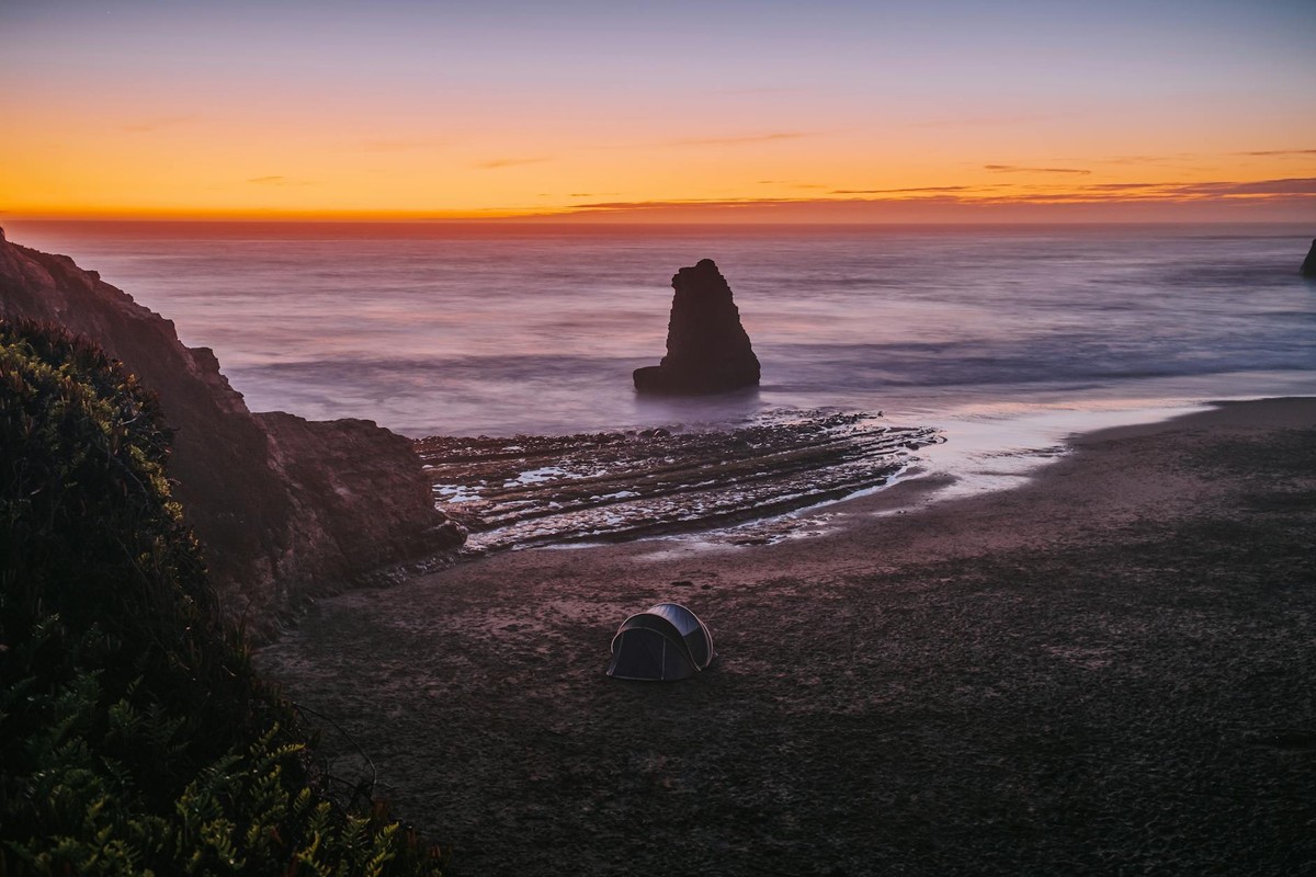 Peaceful sunset view of Davenport Beach, California with a lone tent by the iconic rock formation.