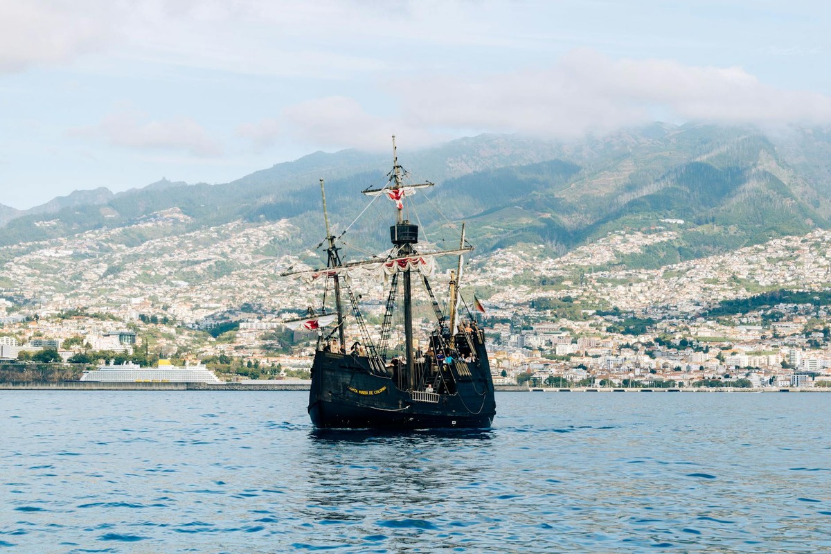 A historic ship sails in Funchal Bay with Madeira's mountains in the backdrop.