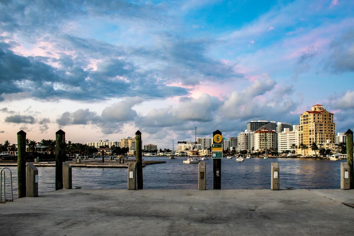 Scenic view of a vibrant waterfront city skyline at sunset with boats and clouds.