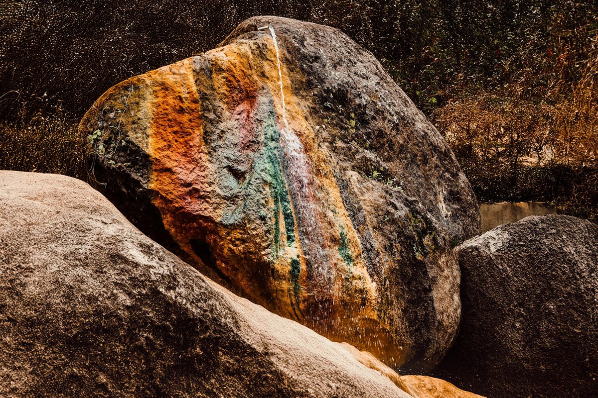 A large boulder outdoors with vibrant mineral streaks creating a colorful natural pattern.