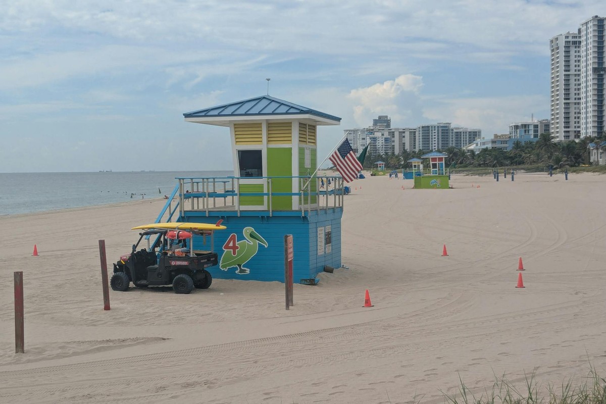 A vibrant lifeguard tower on Pompano Beach, Florida with a clear view of the ocean and nearby buildings in the background.