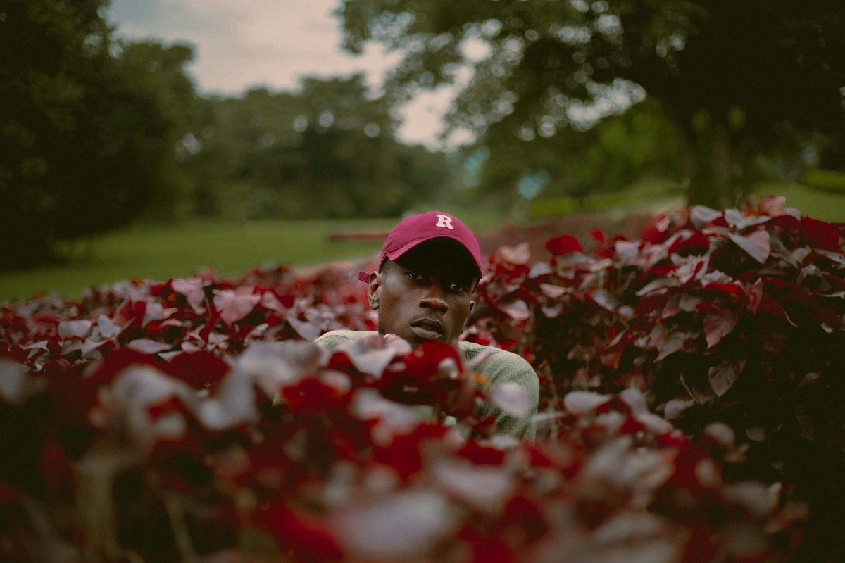 Portrait of a man surrounded by vibrant red flowers in Abuja garden.