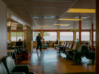 Relaxed passengers on a Seattle ferry with scenic water views. Interior seating and restrooms in view.