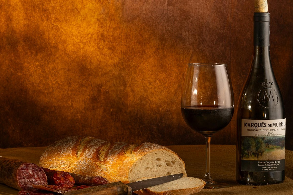 A rustic still life of wine, bread, and charcuterie in a warm setting.