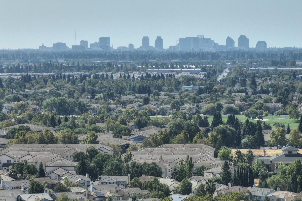 Aerial view of Sacramento's suburban homes with the city skyline in the distance. Lush greenery and clear skies.