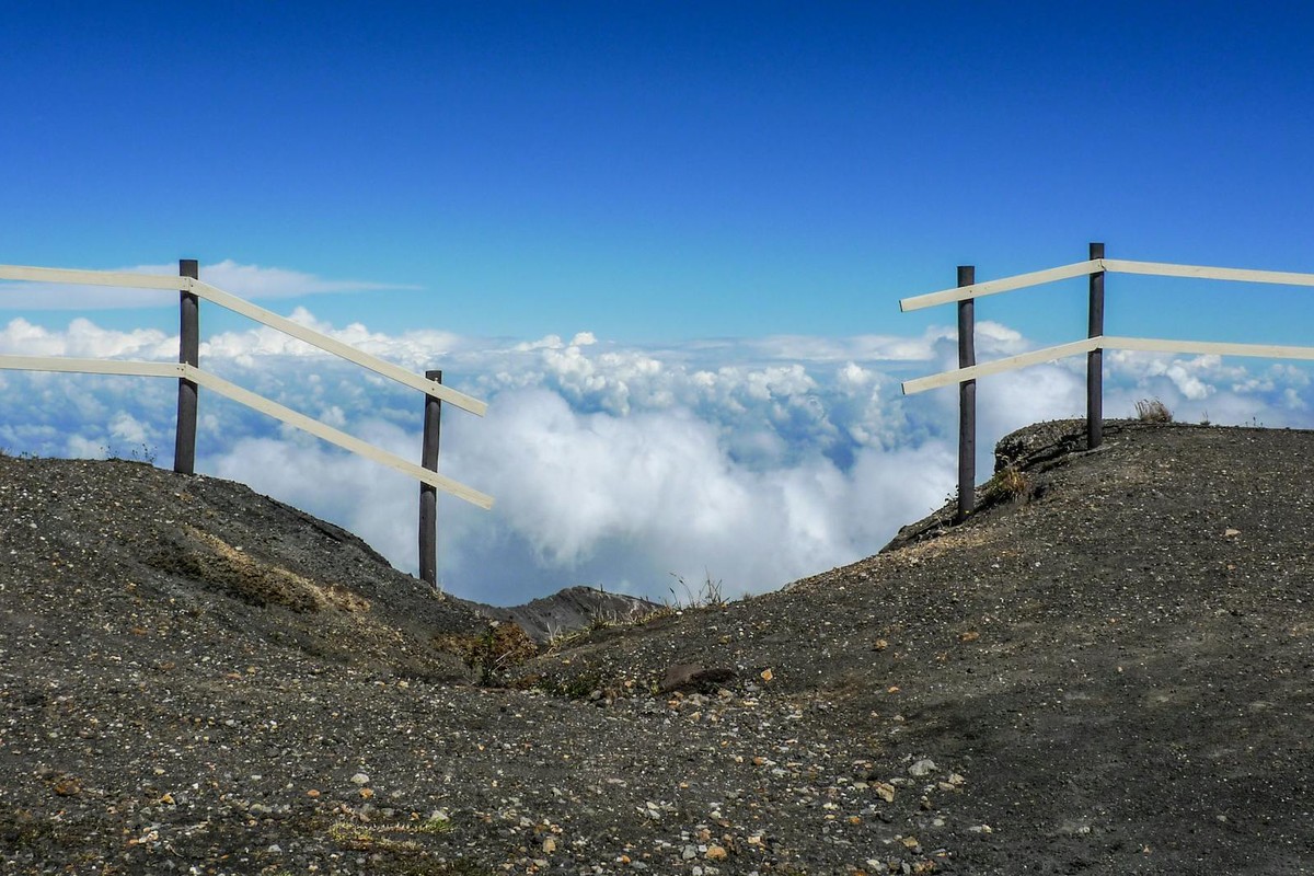 A scenic mountain landscape with a fence overlooking clouds under a clear blue sky.