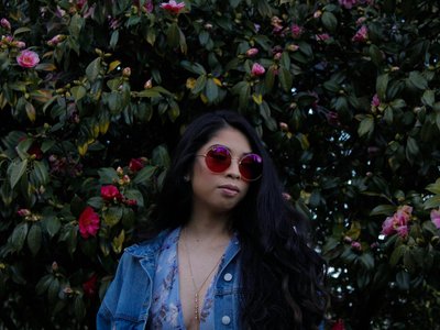 Woman with sunglasses poses in front of blooming flowers wearing a denim jacket in Gresham, OR.