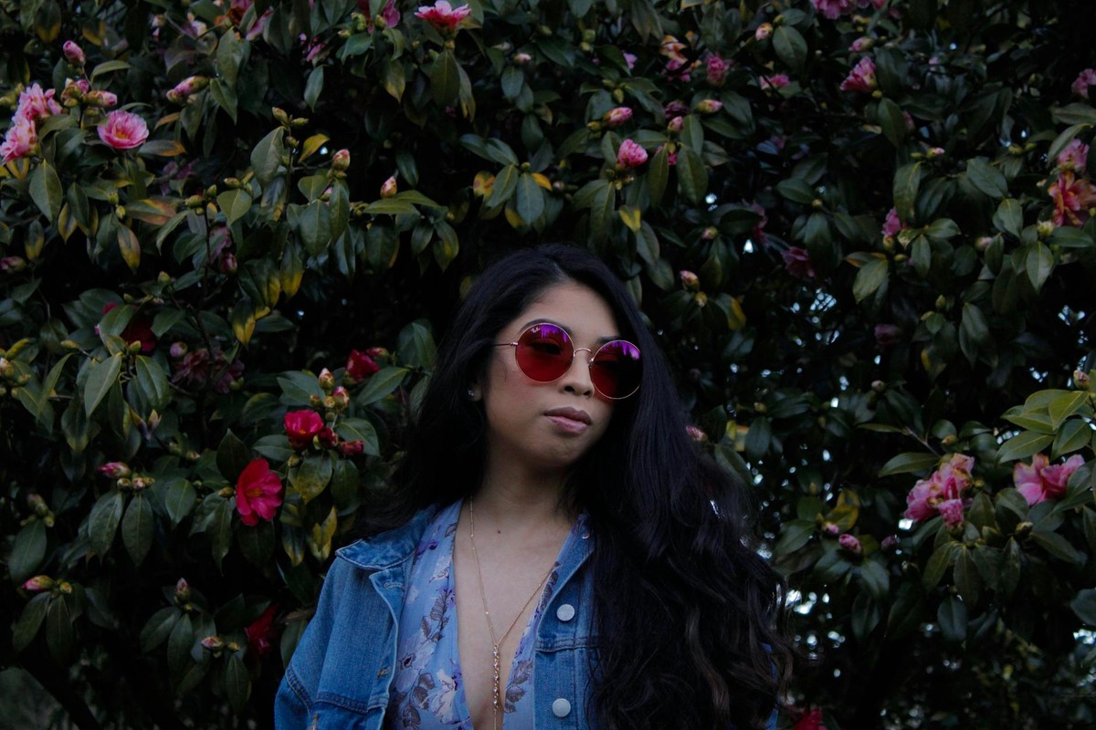 Woman with sunglasses poses in front of blooming flowers wearing a denim jacket in Gresham, OR.