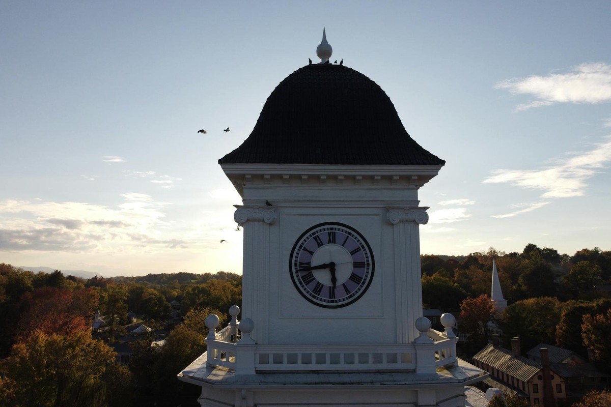 A striking white clock tower captured outdoors during sunset with birds flying nearby.