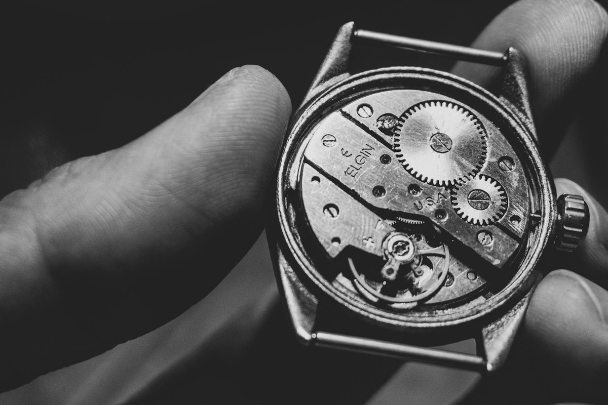 Black and white close-up of a vintage watch mechanism held in hand, showcasing intricate gears.