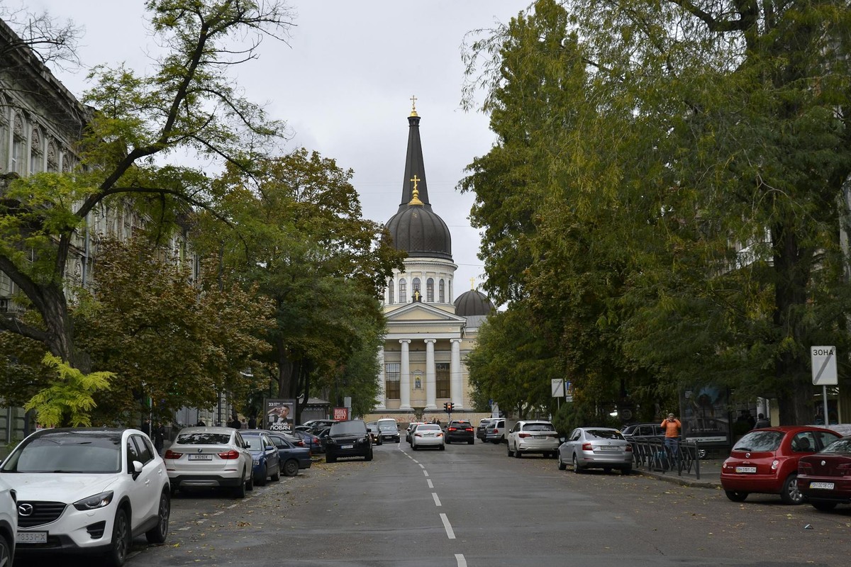 Street view of a cathedral in Odessa, Ukraine with cars parked and trees lining the road.