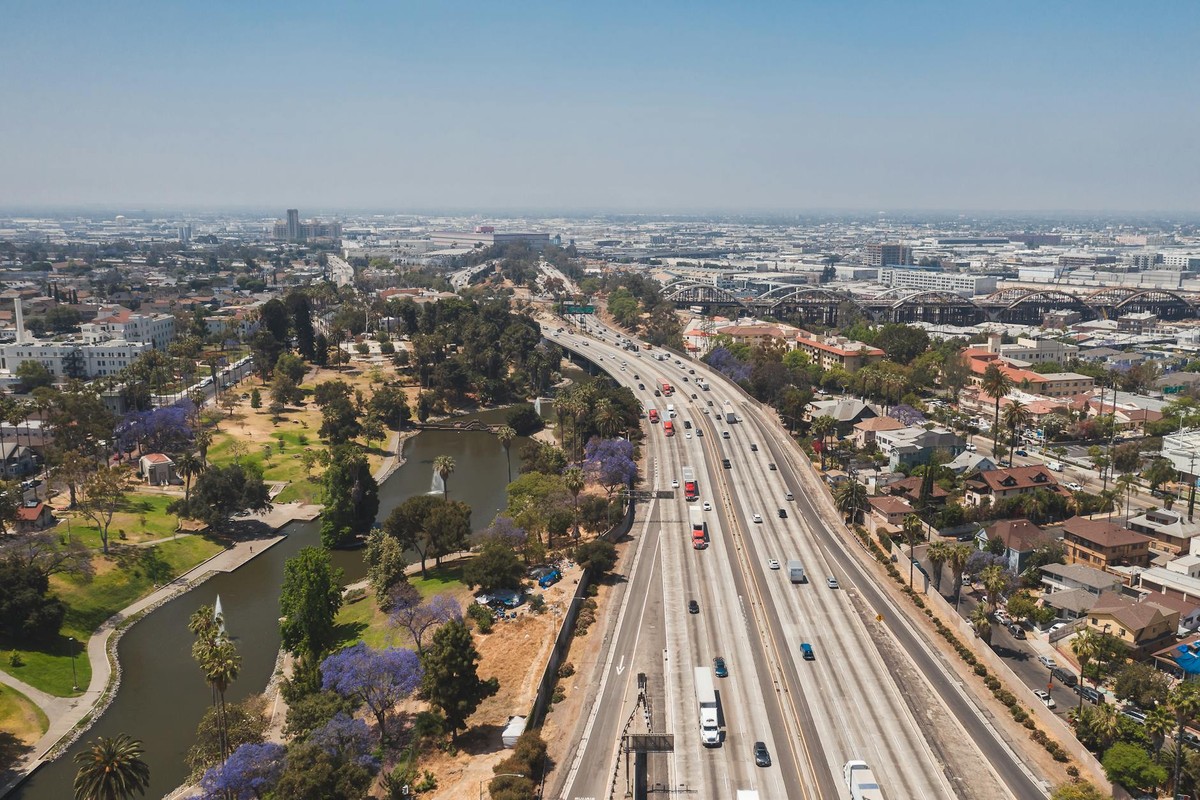 Aerial view of a busy Los Angeles freeway flanked by a verdant park and urban landscape.