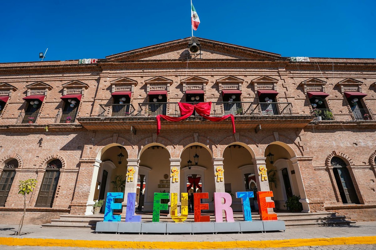 Colorful El Fuerte sign in front of historic municipal building under clear blue sky.