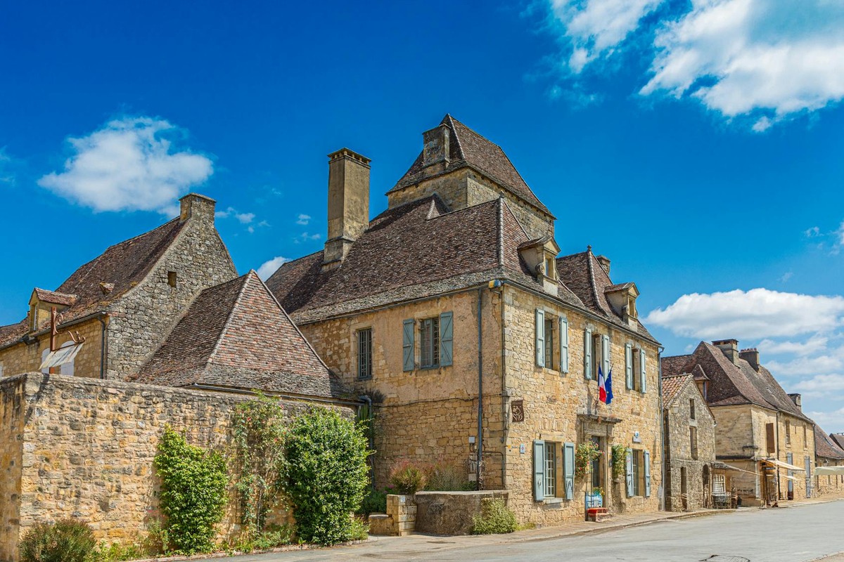 Charming street scene of a historic French village with stone buildings under a blue sky.